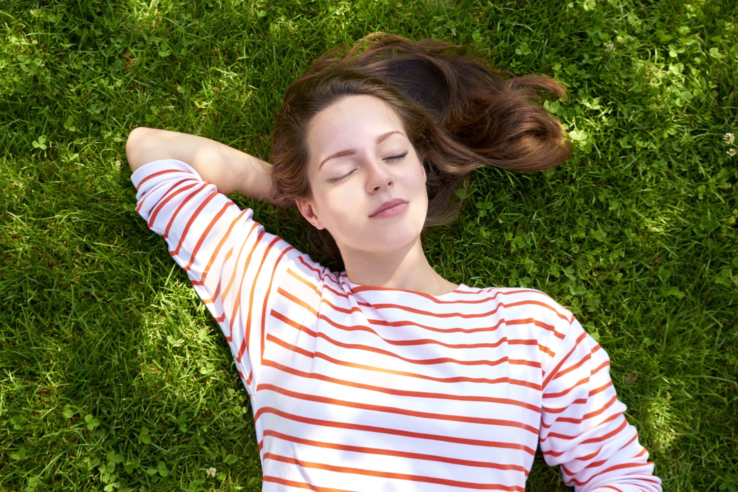 Shot from above of a beautiful young woman with closed eyes lying on grass in summer.