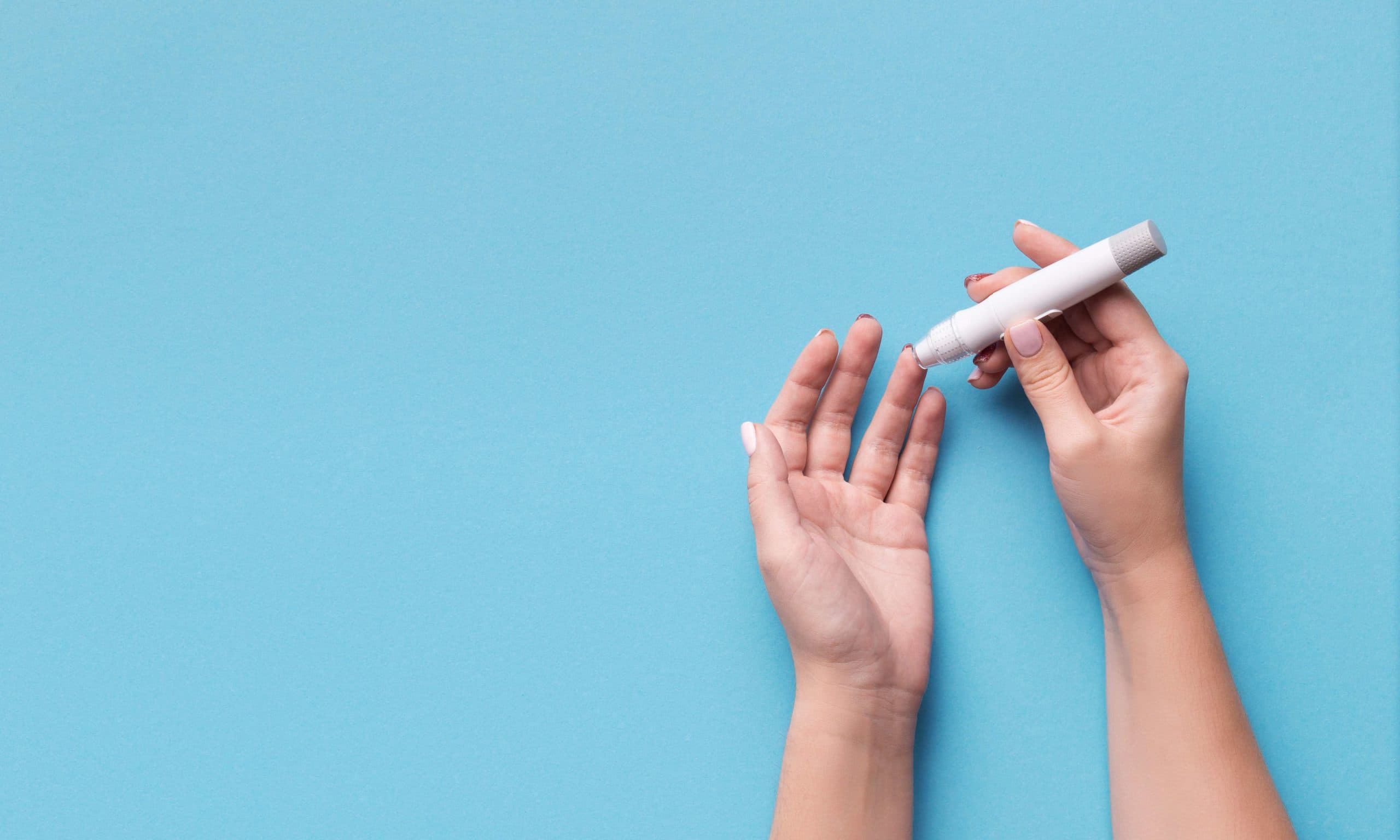 Diabetes test. Woman hands checking blood sugar level by Glucose meter on blue background, copy space