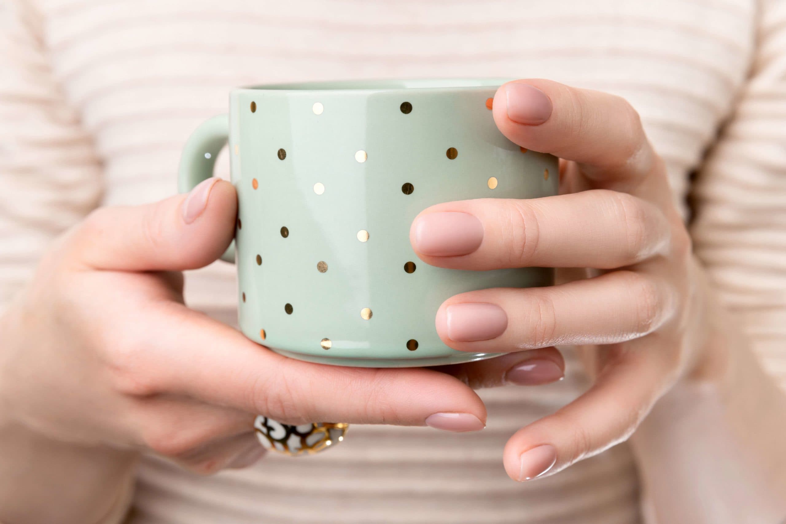 Woman with groomed hands with nude beige pink nail design holding cup. Manicure, fashion and beauty salon concept