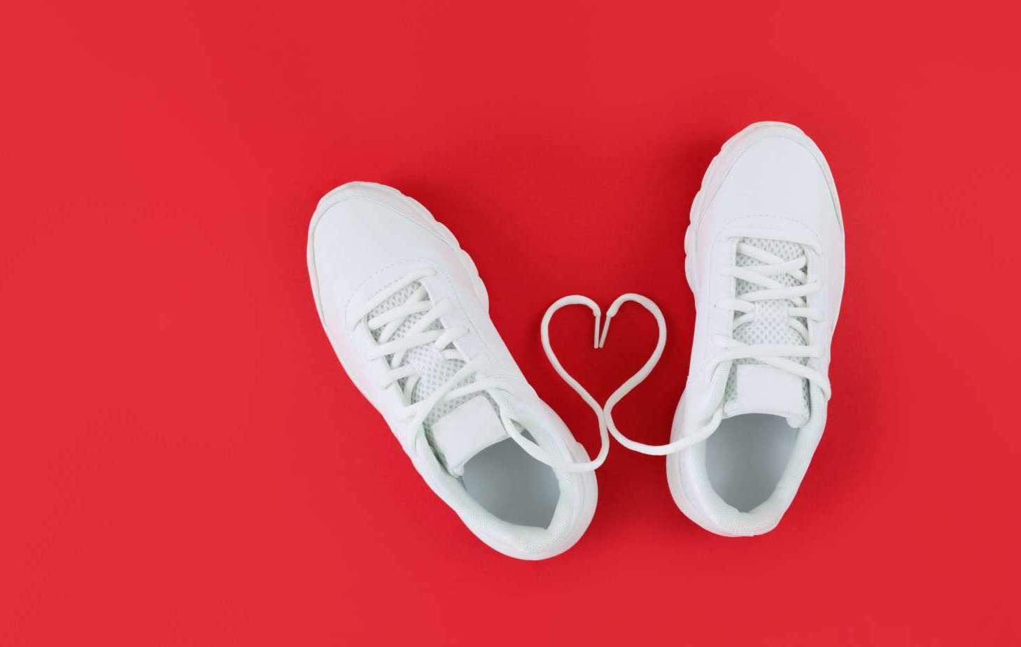 White sports shoes and heart shape from laces on a red background. Simple flat lay banner with copy space.