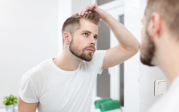 Handsome unshaven man looking into the mirror in bathroom