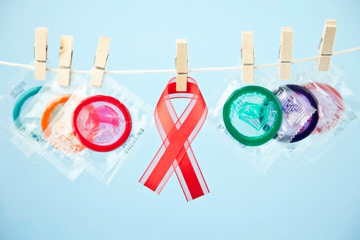Verpackte Kondome und ein AIDS Awareness-Band hängen mit Klammern befestigt an einer Wäscheleine vor hellblauem Hintergrund