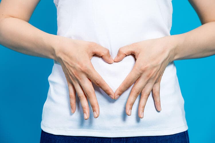 Junge Frau formt mit ihren Händen ein Herz vor ihrem Bauch.