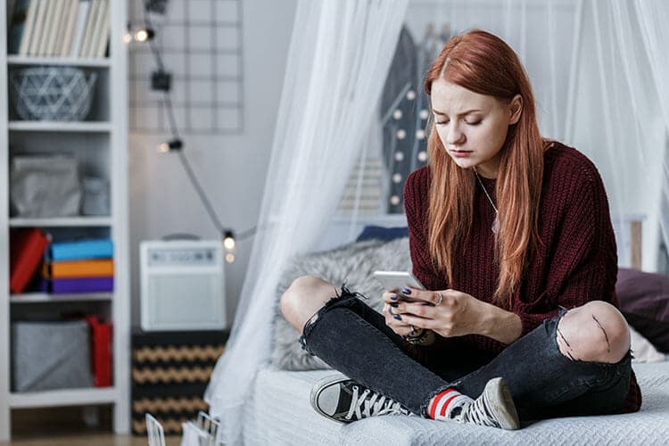 Teenager sitzt auf ihrem Bett und schaut auf das Smartphone.
