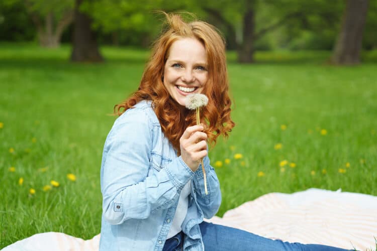 Lachende Frau auf Wiese mit Pusteblume