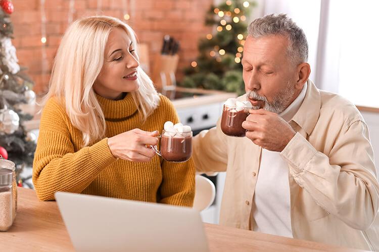 Ein Ehepaar mittleren Alters trinkt einen Kakao vor dem Laptop.