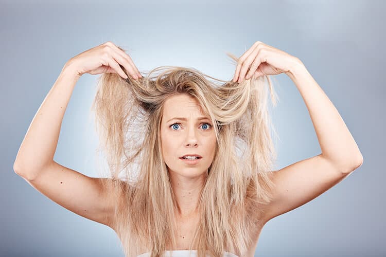 Junge Frau hält sich verwirrt die blonden Haare hoch.