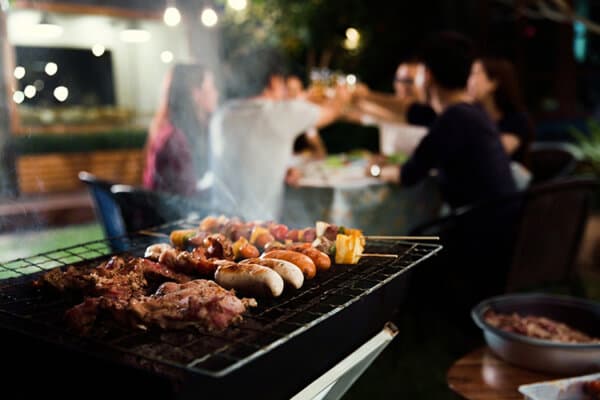 Grill mit sich zu prostenden Freunden im Hintergrund