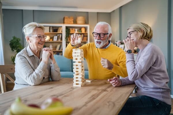 Zwei ältere Frauen und ein Mann spielen im Wohnzimmer Jenga