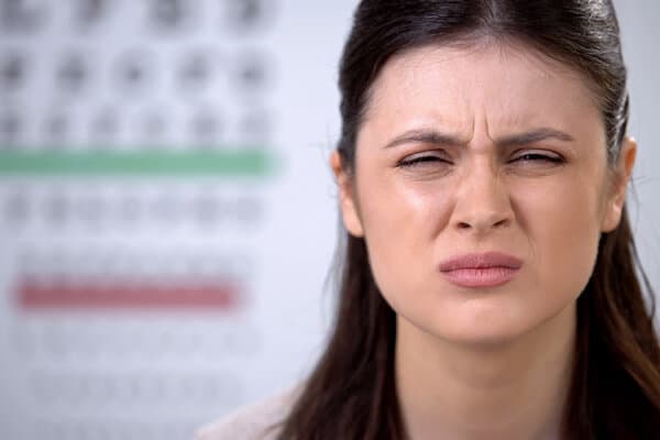 Eine junge dunkelhaarige Frau kneift beim Sehtest verzweifelt die Augen zusammen.