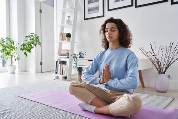 Junge Frau mit dunklen Haaren sitzt im Wohnzimmer und macht Yoga
