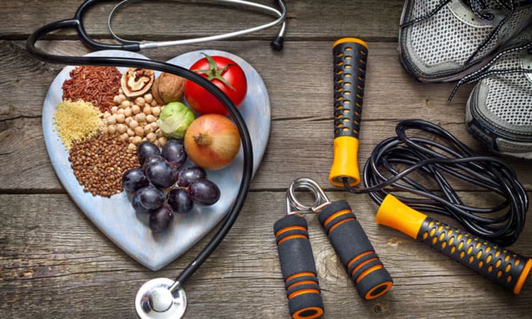 Gesundes Essen auf einer herzförmigen Platte, Stethoskop und Sportartikel auf dunklem Holz-Untergrund