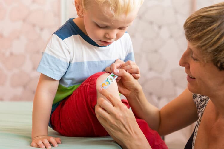 Mutter versorgt Wunde am Knie ihres Sohnes.